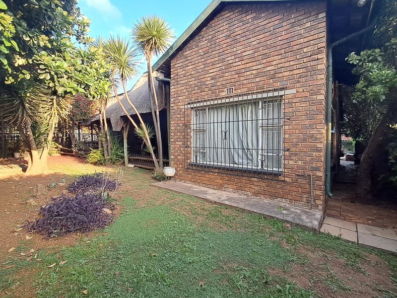 Rear view of the property featuring a face brick facade, security bars on windows, and a thatched roof section overlooking the garden area.