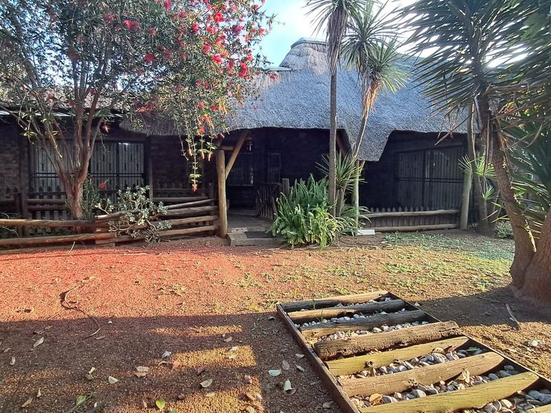 Rear view of a house featuring a traditional thatched roof, timber support structures, and security bars on the windows, set within a garden area.