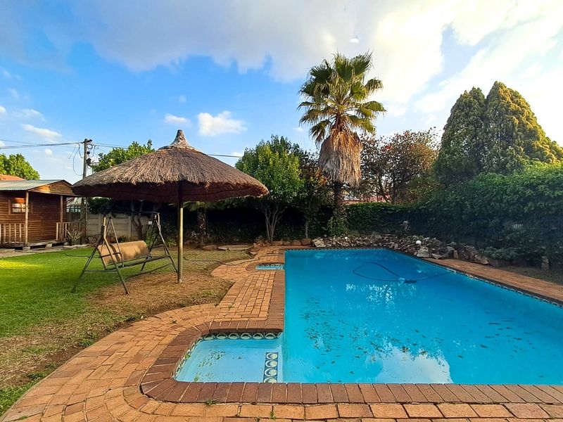 Outdoor pool area featuring a swimming pool with brick coping, surrounded by a lawn and established garden boundary.