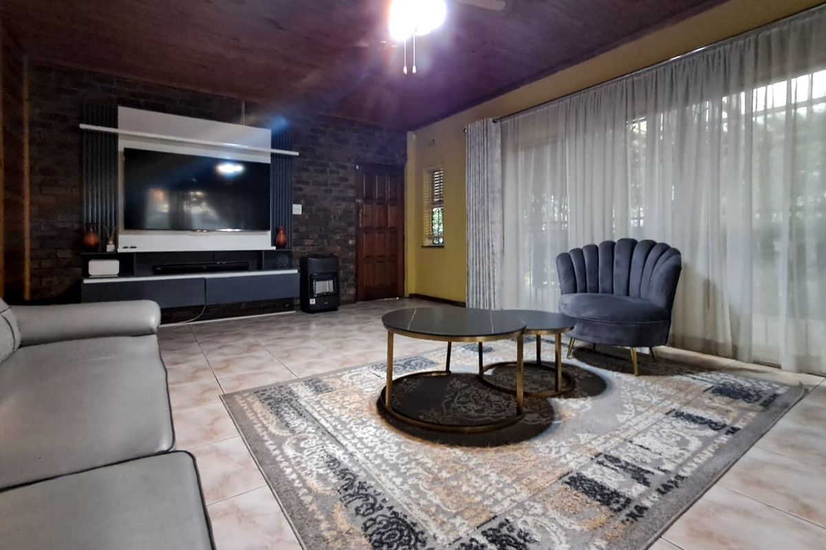 A spacious living room featuring an exposed brick feature wall, timber ceiling, tiled flooring, and large sliding glass doors providing natural light.