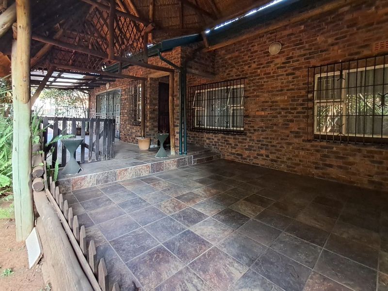 A covered outdoor patio area featuring rustic exposed brick walls, tiled flooring, and a traditional thatched roof structure with timber supports.