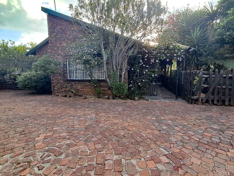 Front exterior view of a brick house featuring a circular pattern cobblestone driveway and established garden surroundings.
