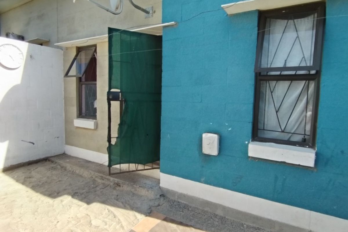 Rear exterior view of the property featuring painted masonry walls, casement windows, and a security gate entrance.