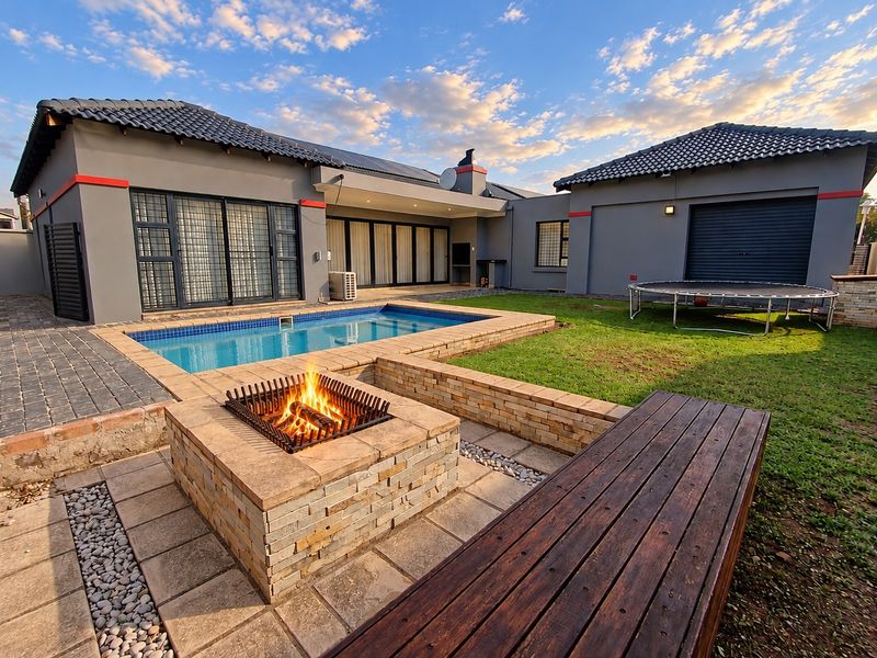 A well-maintained rear exterior featuring a swimming pool, stone-clad fire pit, and paved patio area, perfect for outdoor entertaining.