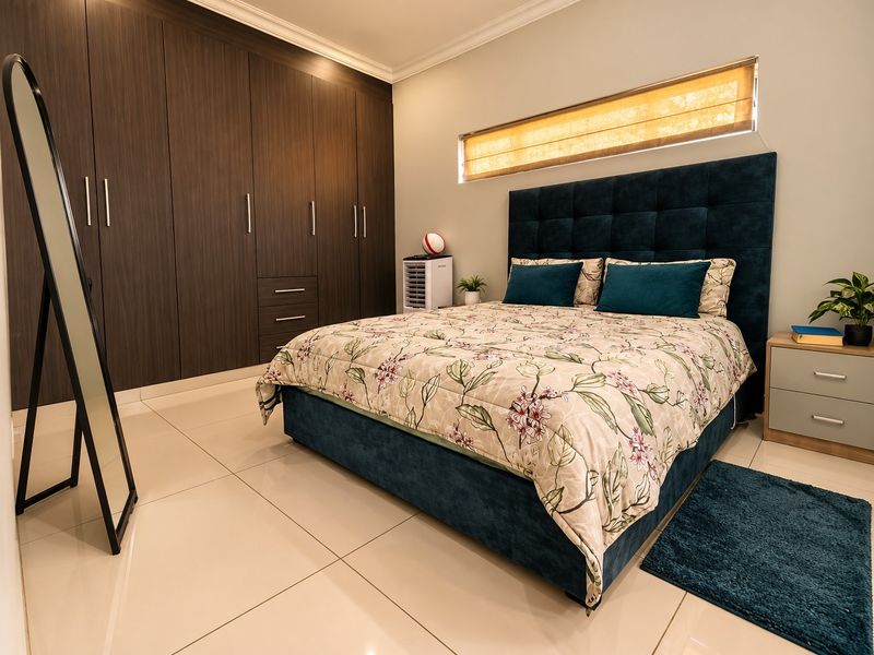 A well-maintained bedroom featuring large dark wood built-in cupboards, sleek tiled flooring, and a modern horizontal clerestory window for natural light.