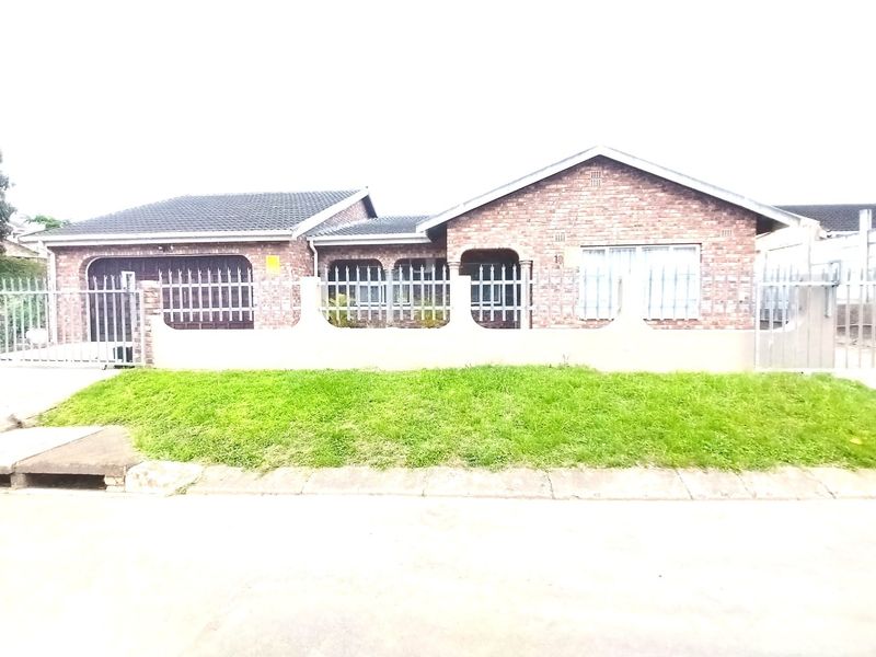 Front elevation of a single-story face brick house featuring a tiled roof, perimeter wall with security fencing, and a paved driveway.