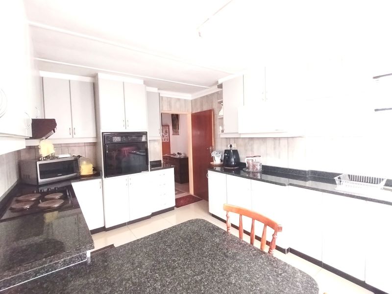 A functional kitchen featuring white cabinetry, dark granite countertops, built-in oven, and electric hob with tiled finishes.