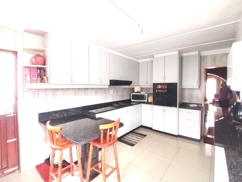 A functional kitchen featuring white cabinetry, dark granite countertops, a built-in oven, hob, and a breakfast nook area with tiled flooring.