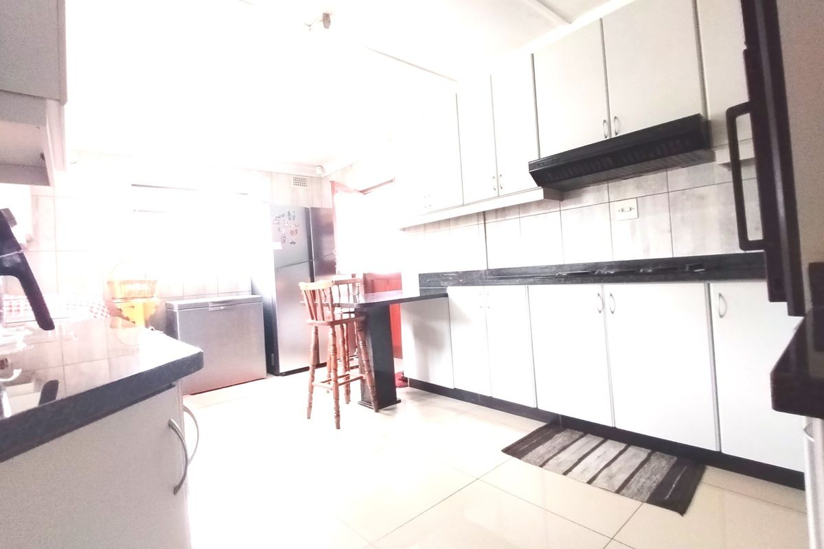 A functional kitchen featuring white cabinetry, dark granite countertops, tiled flooring, and a built-in extractor fan.