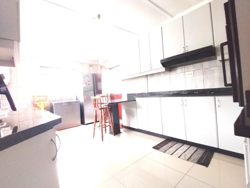 A functional kitchen featuring white cabinetry, dark granite countertops, tiled flooring, and a built-in extractor fan.