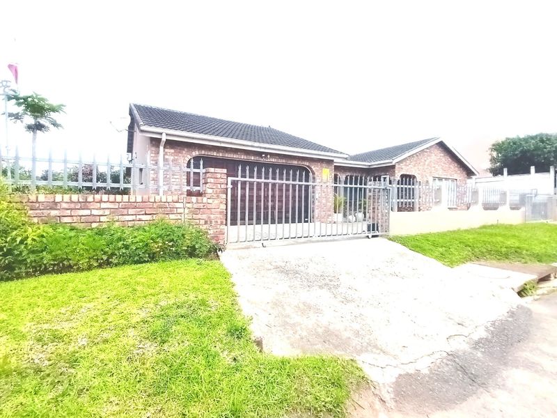 Front view of a face brick house featuring a tiled roof, concrete driveway, and secure metal perimeter fencing.