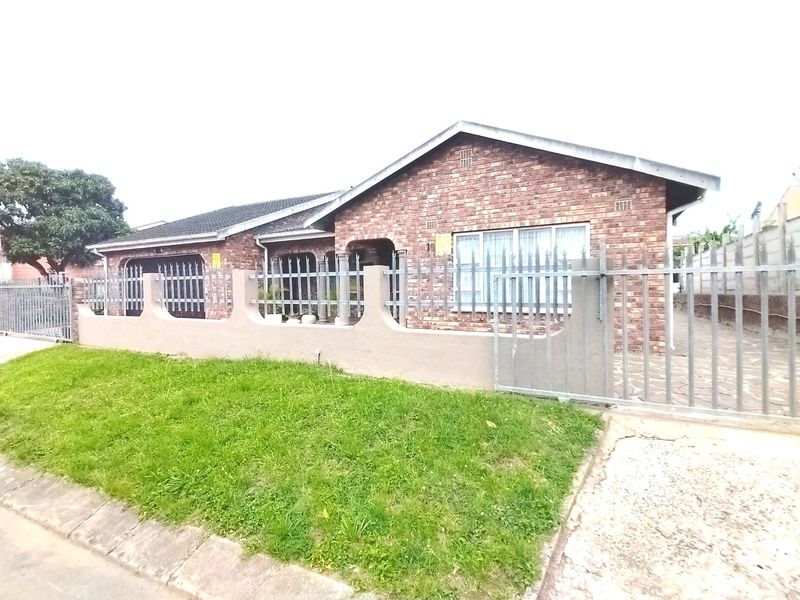 Front view of a single-story face brick house featuring a paved driveway, metal security fencing, and a gated entrance.