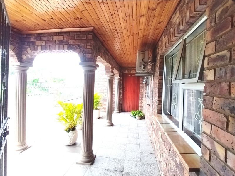 A covered patio area featuring exposed brick walls, classic columns, a timber ceiling, and tiled flooring, providing a sheltered outdoor space.