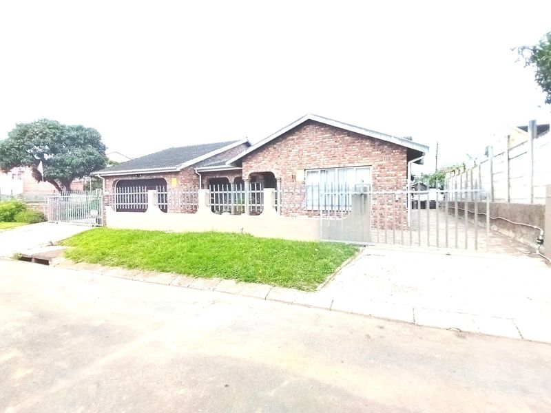 Front view of a single-story face brick house featuring a tiled roof, metal perimeter fencing, and a paved driveway.