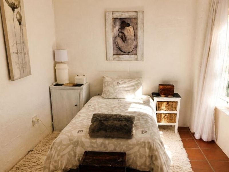 A cozy bedroom featuring terracotta floor tiles and a large multi-pane window that allows for natural light.