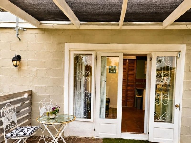 A covered patio area featuring a shade cloth pergola, brick paving, and access to the interior through white french doors with security grilles.