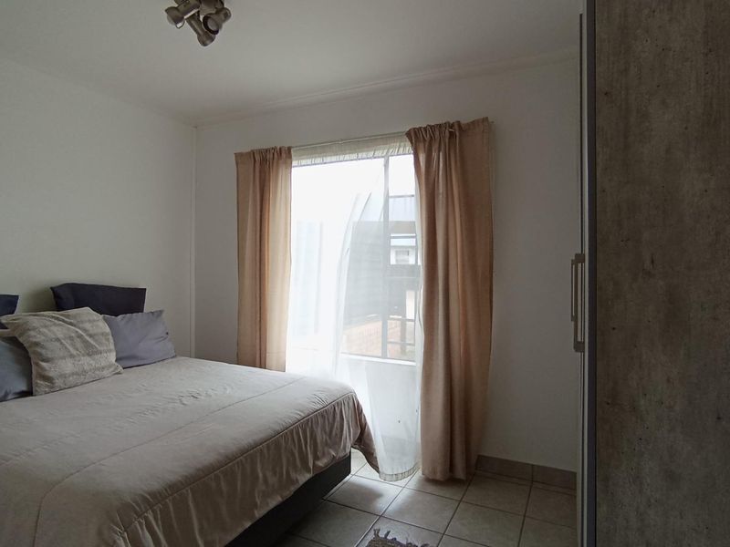 A functional bedroom featuring tiled flooring, a built-in wardrobe, and natural light through a window with curtains.