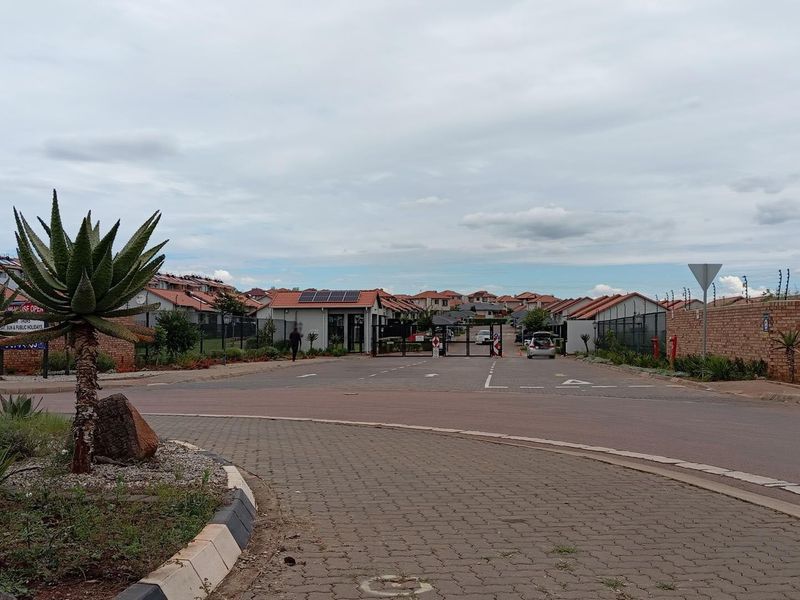 Street view of a residential apartment complex entrance featuring paved roads, brick boundary walls, and secure gated access.