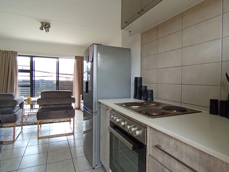 Open-plan kitchen and living area featuring modern cabinetry, built-in oven and hob, tiled flooring, and access to an outdoor space via sliding doors.