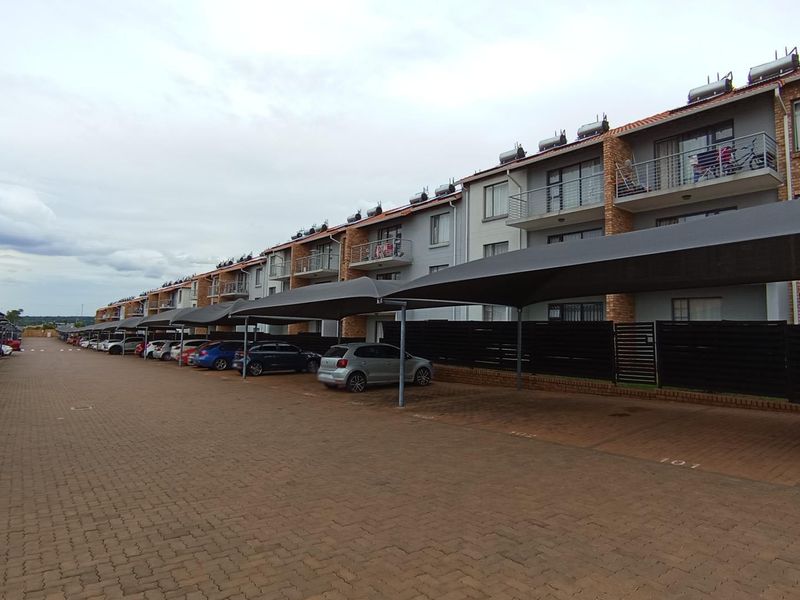 Exterior view of a multi-story apartment complex featuring brick and plaster facade, private balconies, and dedicated covered parking bays for residents.
