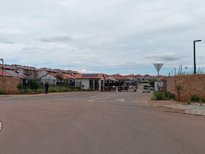 Street view of a residential complex entrance featuring brick boundary walls, electric fencing, and solar-equipped housing units.
