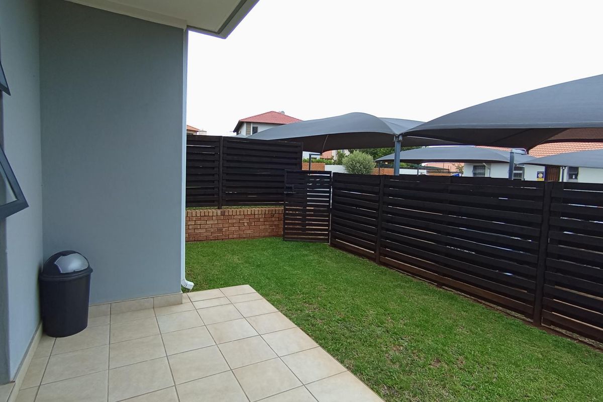 A private rear garden featuring a tiled patio area, well-maintained lawn, and secure timber slat fencing with overhead shade sails.
