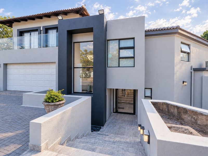 Modern double-story residence featuring a contemporary facade, paved driveway, double garage, and an elegant stone-tiled entrance staircase with glass balustrades.
