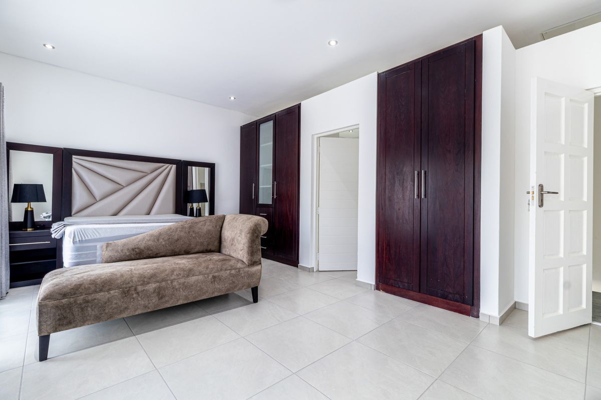 Spacious bedroom featuring neutral tiled flooring, recessed downlighting, and extensive dark wood built-in cabinetry providing ample storage space.