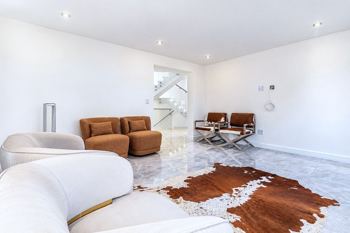 A bright, modern living area featuring polished marble flooring, recessed downlighting, and a clear view through to a contemporary staircase with a glass balustrade.