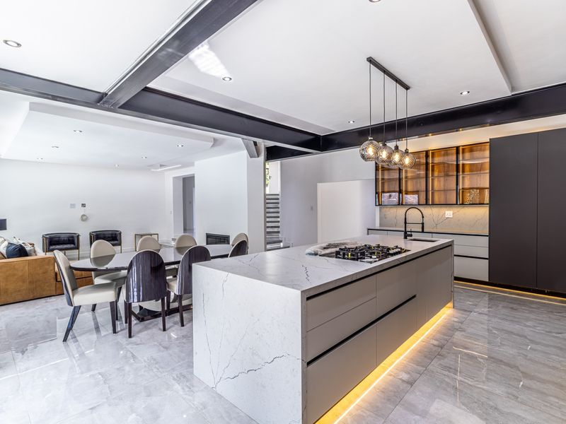 Modern open-plan living and kitchen area featuring a large stone-topped island, sleek cabinetry, exposed steel beams, and high-end finishes throughout.