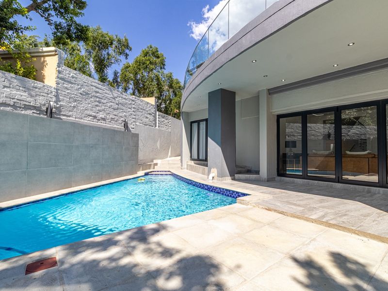 Modern outdoor pool area featuring a tiled patio, glass balustrade, and seamless access to the interior through large sliding glass doors.