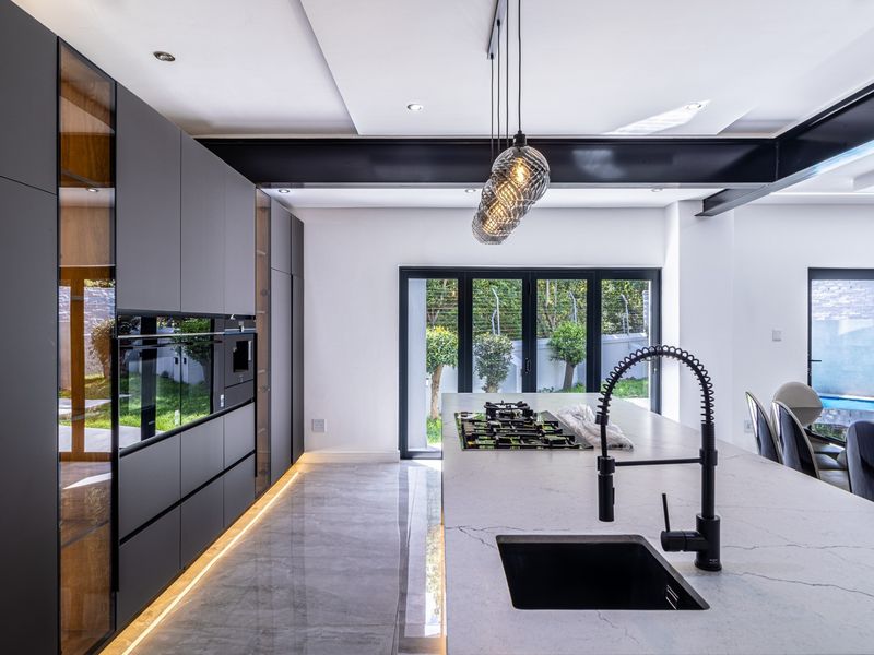 Modern open-plan kitchen featuring sleek matte cabinetry, a large stone-topped island with integrated gas hob, and direct access to the garden through bi-fold doors.