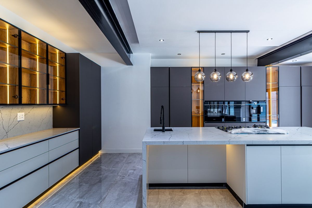 Modern luxury kitchen featuring a large stone-topped island, integrated high-end appliances, sleek dark cabinetry, and sophisticated ambient lighting throughout.