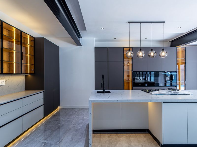 Modern luxury kitchen featuring a large stone-topped island, integrated high-end appliances, sleek dark cabinetry, and sophisticated ambient lighting throughout.