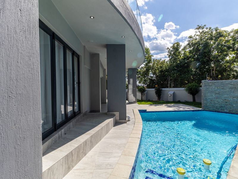 A modern outdoor pool area featuring a tiled patio, glass balustrade, and a stone-clad feature wall, perfect for outdoor relaxation and entertainment.