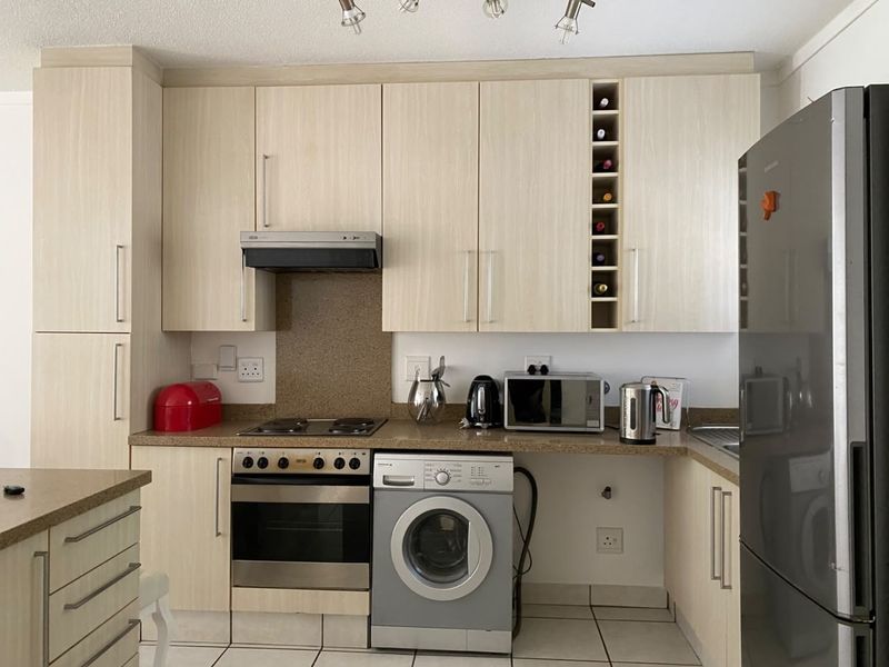 A functional kitchen featuring light wood-finish cabinetry, integrated appliances including an oven and stove, and tiled flooring with ample counter space.