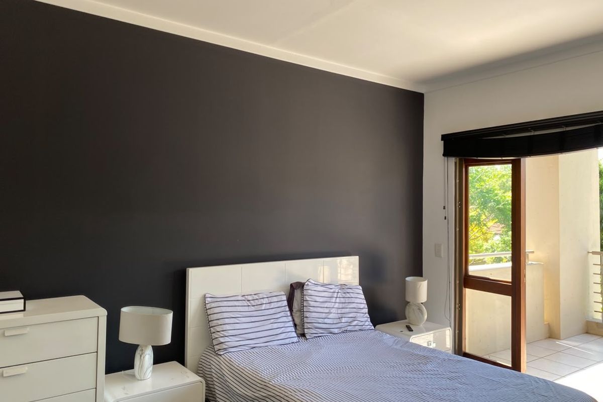 A well-maintained bedroom featuring a dark accent wall and direct access to a private balcony through a glass door.