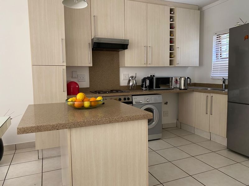 A functional kitchen featuring light wood-finish cabinetry, stone countertops, integrated appliances, and tiled flooring, offering a clean and practical workspace.
