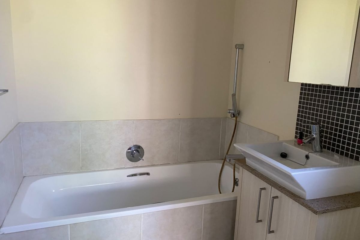 A functional bathroom featuring a built-in bathtub, vanity cabinet with basin, and wall-mounted mirror with tiled splashback finishes.