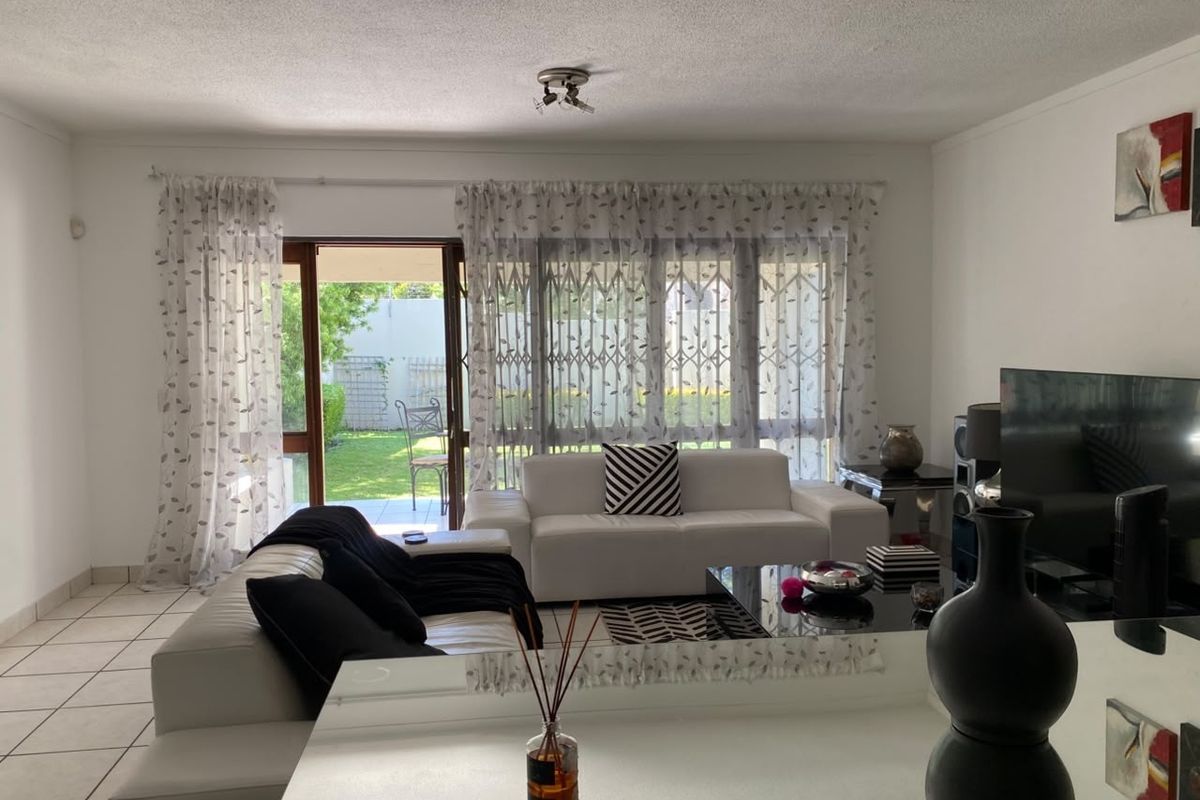 A bright living room featuring tiled flooring and a large sliding glass door providing direct access to the rear garden area.