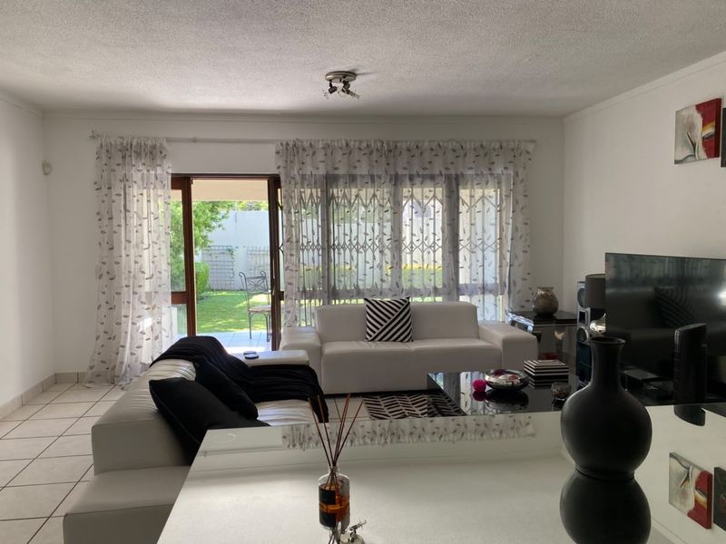 A bright living room featuring tiled flooring and a large sliding glass door providing direct access to the rear garden area.