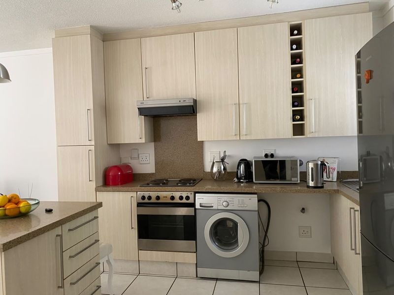 Functional kitchen featuring light wood-grain cabinetry, stone countertops, built-in oven, electric hob, extractor fan, and dedicated space for a washing machine.
