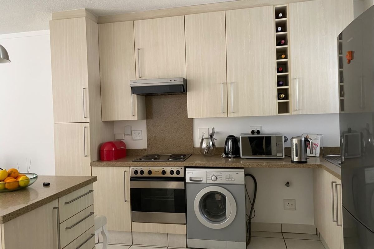 Functional kitchen featuring light wood-grain cabinetry, stone countertops, built-in oven, electric hob, extractor fan, and dedicated space for a washing machine.