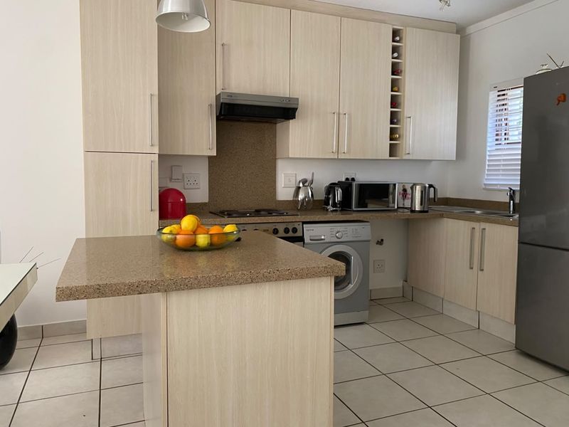 Functional kitchen featuring light wood-grain cabinetry, stone-look countertops, integrated wine storage, and tiled flooring, providing a practical layout for daily meal preparation.