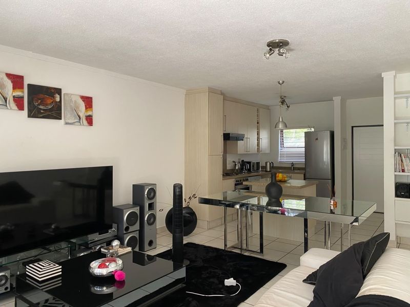 Open-plan living and kitchen area featuring tiled flooring, neutral cabinetry, and integrated kitchen appliances, creating a functional and connected living space.