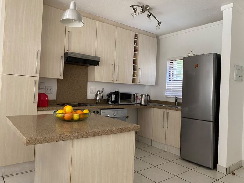 Functional kitchen featuring light wood-grain cabinetry, stone-look countertops, integrated hob, extractor fan, and tiled flooring with a practical layout.