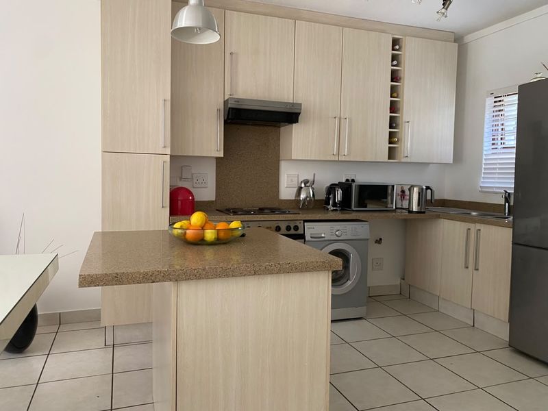 Functional kitchen featuring light wood-tone cabinetry, stone-look countertops, integrated appliances, and tiled flooring, offering a practical layout for daily meal preparation.