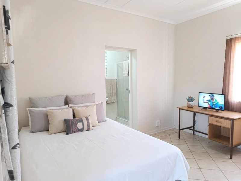 A functional bedroom featuring tiled flooring and an attached en-suite bathroom with a shower enclosure.