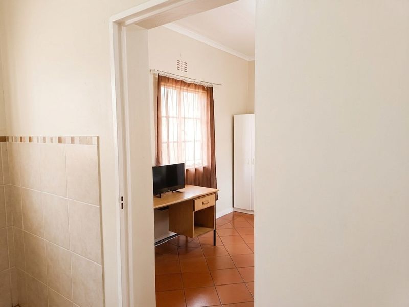 A bedroom featuring terracotta floor tiles and a built-in wardrobe, viewed through a doorway from an adjacent tiled area.