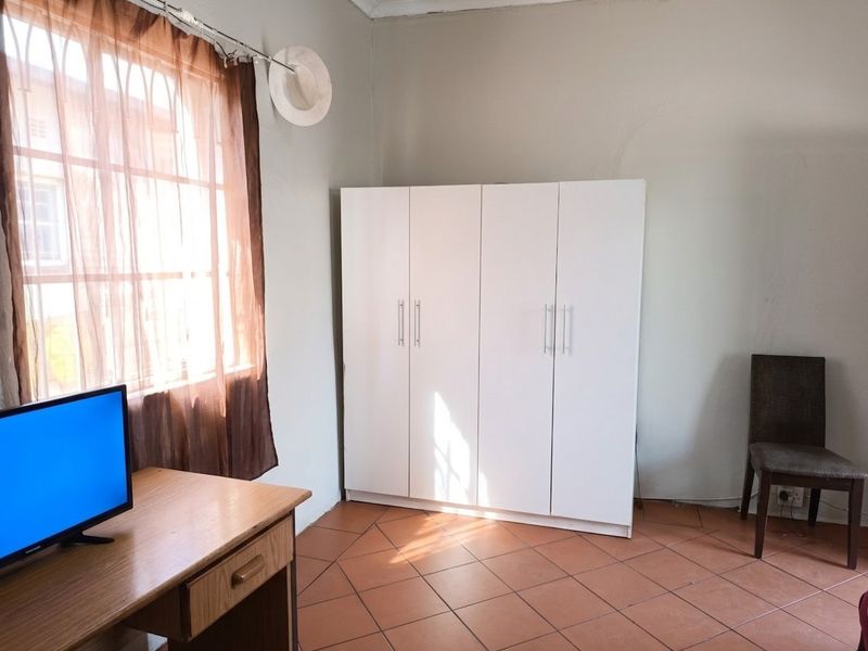 A bedroom featuring tiled flooring and a white built-in wardrobe, offering a functional space with natural light from the window.